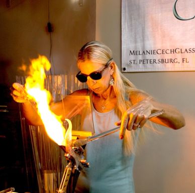 A woman working with molten glass and flames in a glassblowing studio.