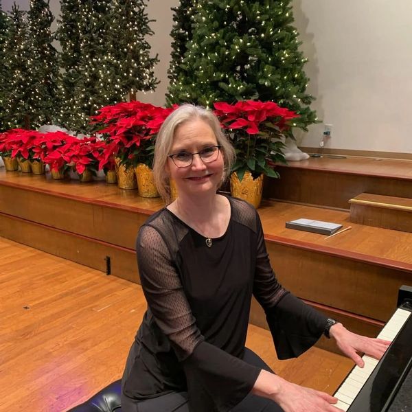 Woman playing piano with Christmas trees and poinsettias in background.