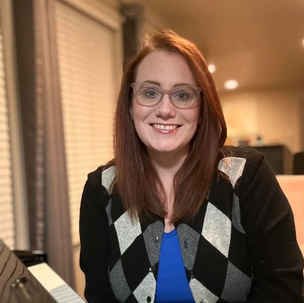 Smiling woman with glasses in a black and gray argyle sweater indoors.