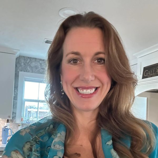 Smiling woman with long hair wearing a floral blue shawl in a kitchen.