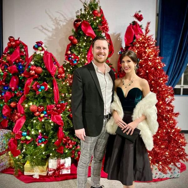 Couple dressed elegantly in front of decorated Christmas trees with gifts.