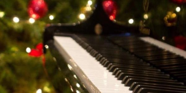 Close-up of piano keys with Christmas tree lights and ornaments in the background.