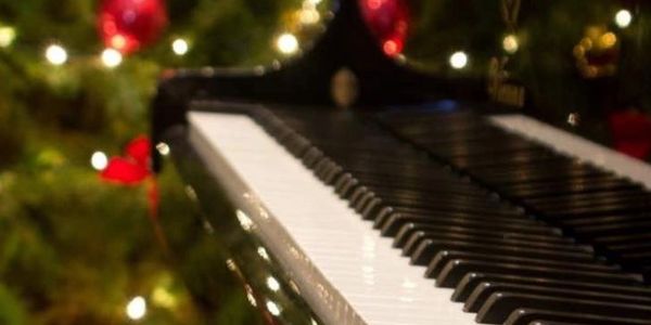 Close-up of piano keys with Christmas tree lights and ornaments in the background.