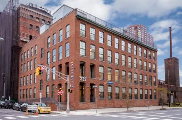 A red brick industrial building on a city street corner with large windows.