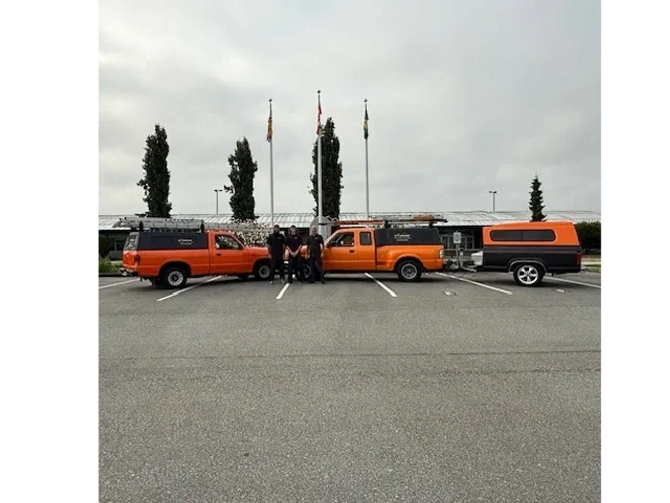 A crew stands together between two orange trucks with camper shells and an orange trailer.
