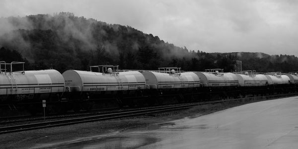 Black and white image of a train with tanker cars on a rainy day.