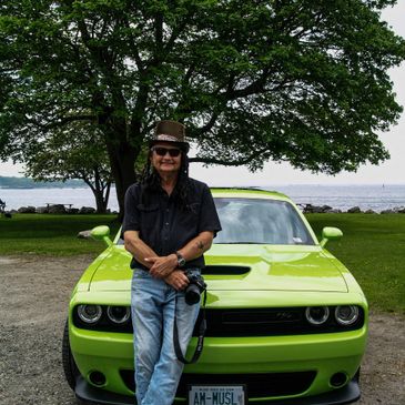 Man leaning against a bright green muscle car with a camera.