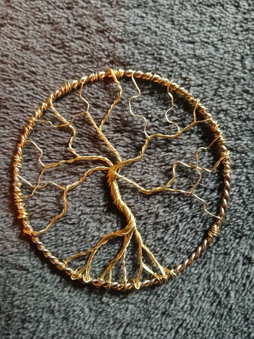 Gold wire tree of life pendant on a dark textured background.