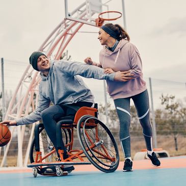 Male wheelchair user playing basketball in his specialed wheelchair with a able bodied female.