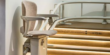 Beige stairlift chair installed on curved staircase with wooden steps.