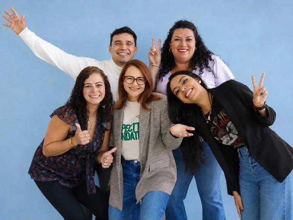 Grupo de cinco personas sonriendo y haciendo gestos de paz y pulgar arriba.
