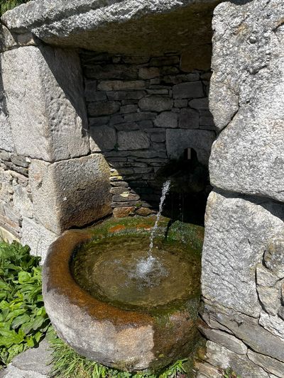 Old stone water fountain with water flowing into a basin.