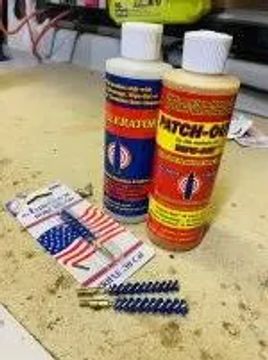 Two bottles of gun cleaning solvent and brushes on a workbench.