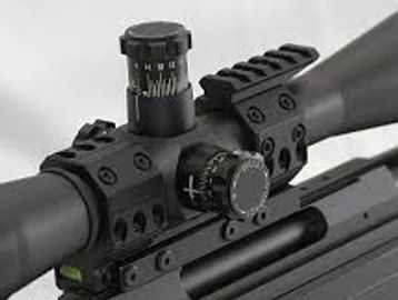 Close-up of a rifle scope with adjustment knobs and mounting rail.