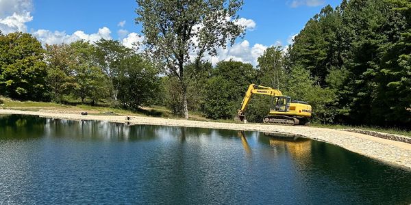 Yellow excavator near a lake under blue sky.