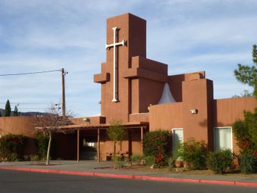 Brown adobe church with a tall tower and cross.