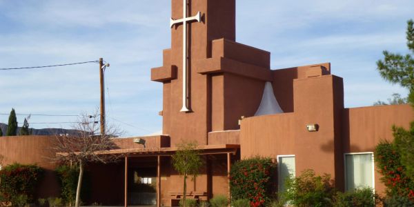 Brown adobe church with a tall tower and cross.