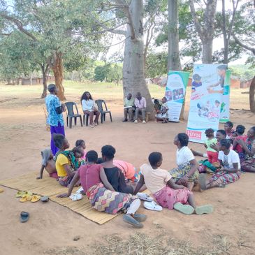 Community members gathered outdoors for an educational session under trees.