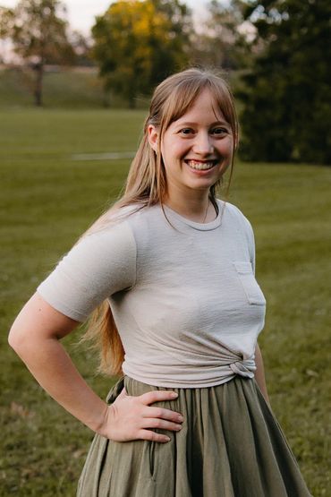 Smiling woman posing outdoors in casual outfit with hands on hips.