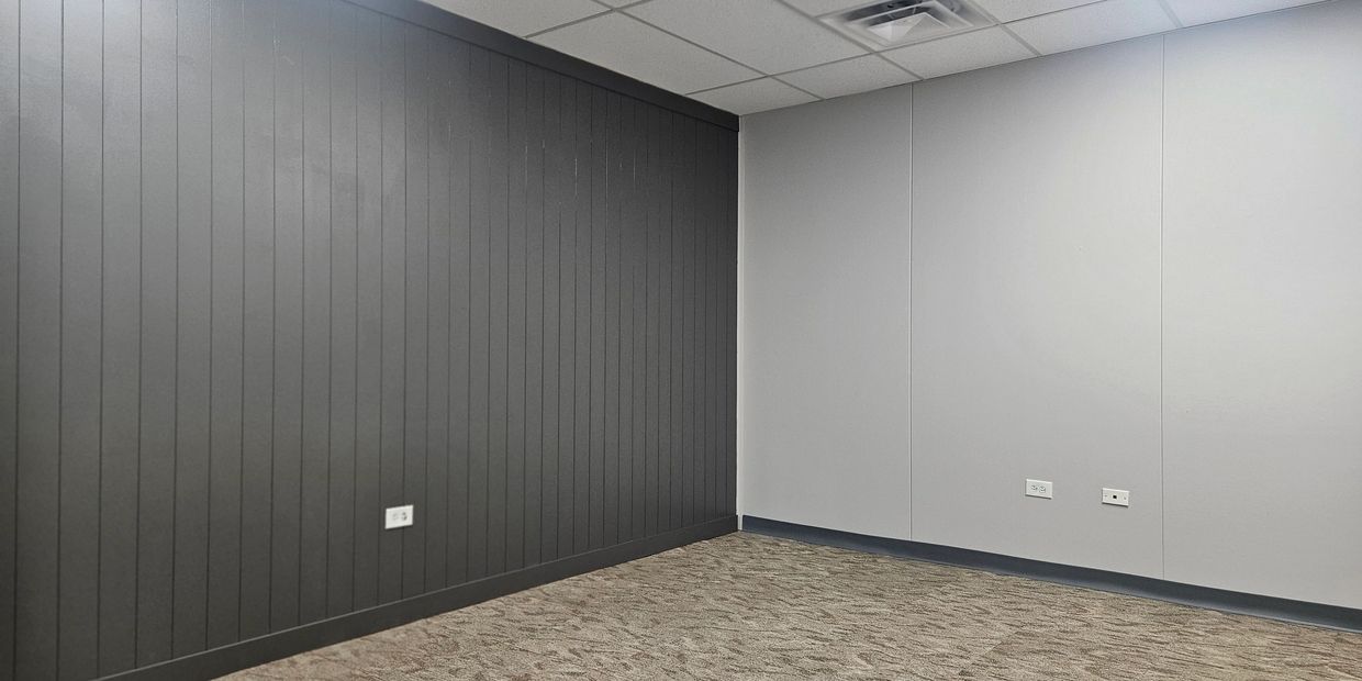 Empty room corner with dark gray and light gray walls and carpeted floor.
