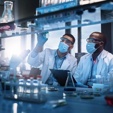 Two scientists in masks and goggles examining a petri dish in a lab.