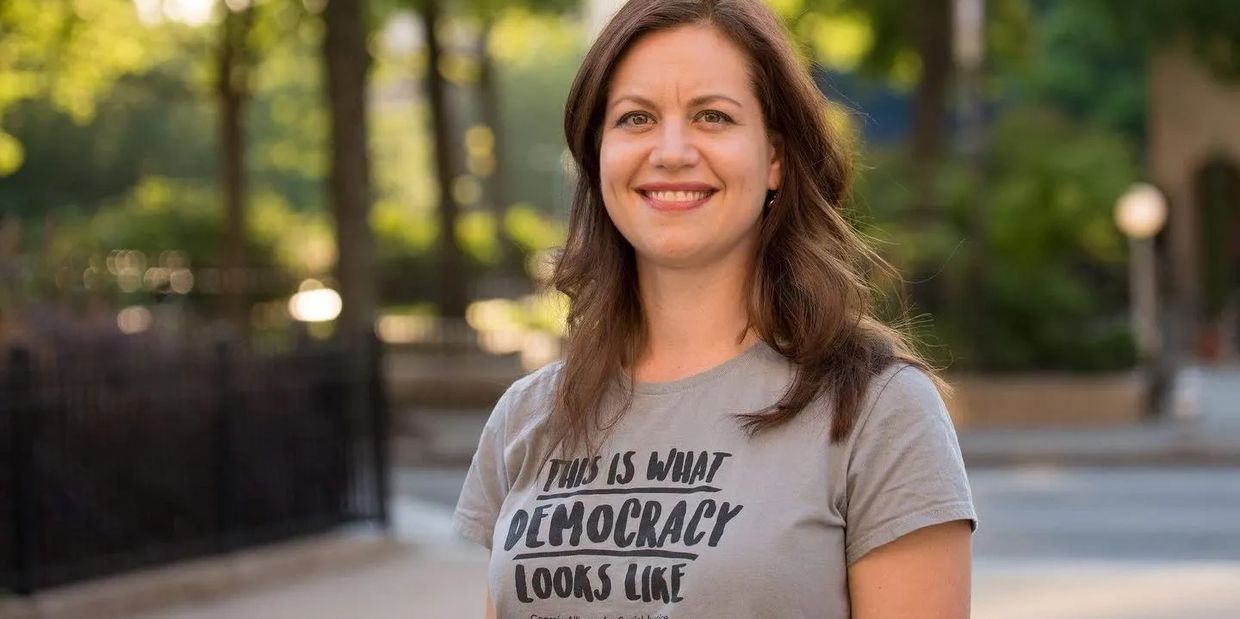 Woman standing, smiling at camera. Her t-shirt reads "This is what Democracy looks like."