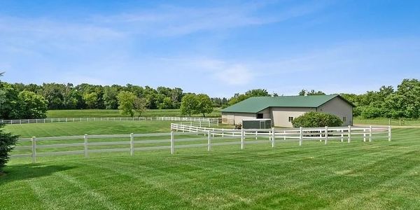 A large green field with white fences and a barn under a clear blue sky.