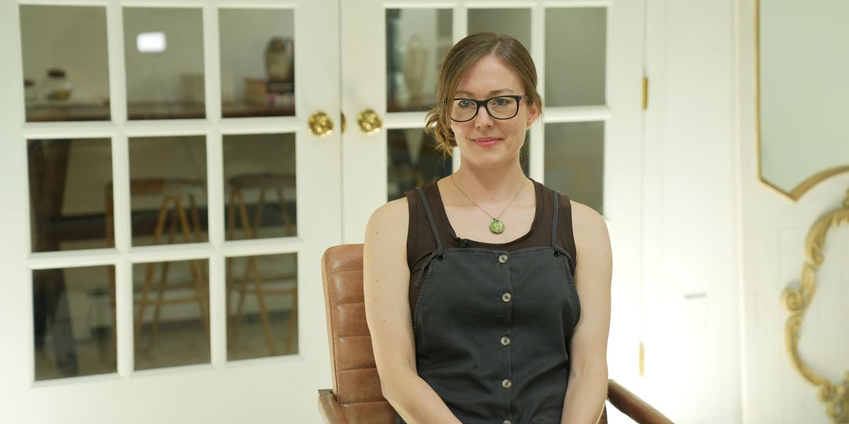 A woman with glasses sitting on a chair in a bright room.
