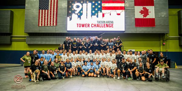 Large group poses at 9/11 Tucson Arena Tower Challenge event with US and Canadian flags.