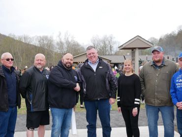 Group of seven people posing outdoors in casual attire, some shaking hands.