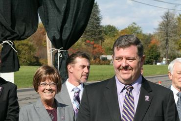 Group of professionals at an outdoor press conference with microphones and a podium.