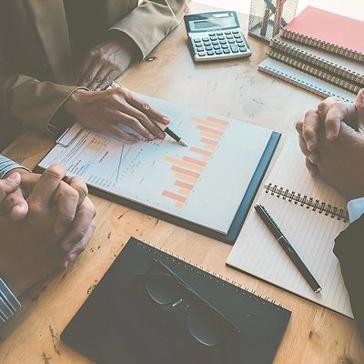 A team of business professionals reviews a document with charts and graphs on a wooden table.