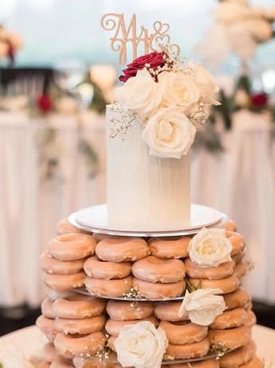 Wedding cake topped with white roses and surrounded by glazed donuts.