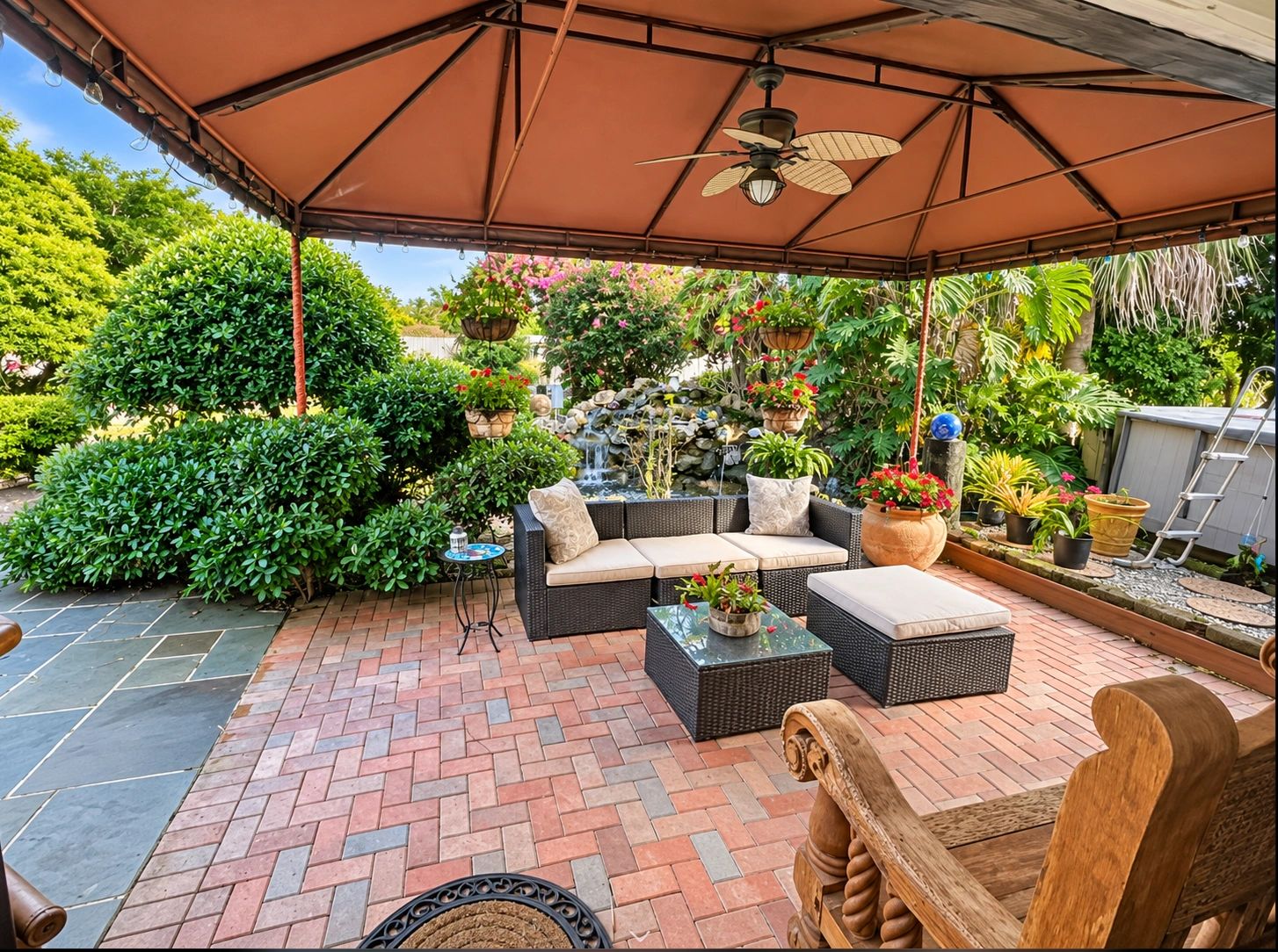 Covered backyard patio with seating, lush tropical landscaping and garden waterfall.