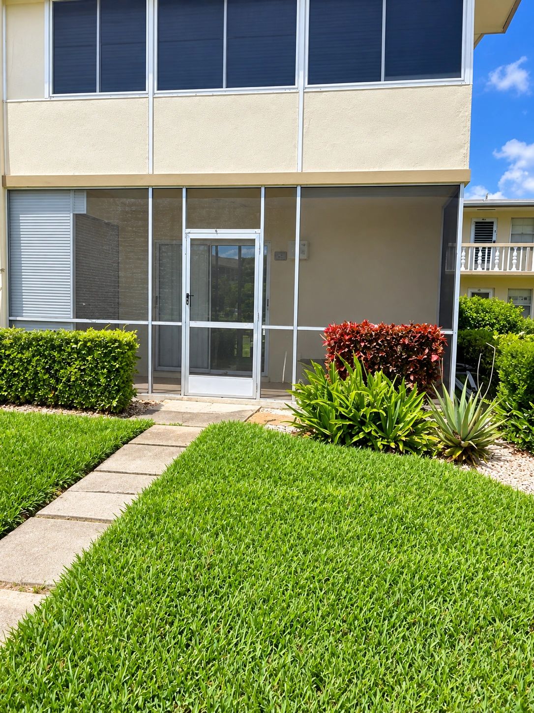 South Florida condo with screened patio, walkway, and landscaped front lawn.