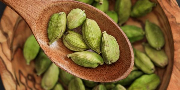 Green cardamom pods on a wooden spoon.