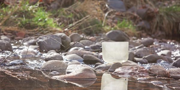 A yellow crystal singing bowl sitting amidst stones by a stream.