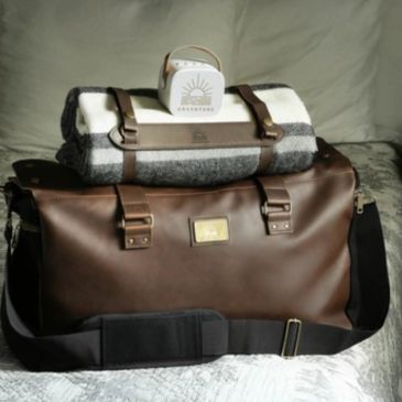 A stylish leather bag with a rolled blanket and a small box on top.