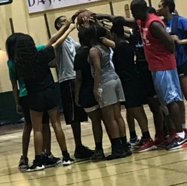 A group of young basketball players forming a huddle with hands together.