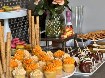Table filled with desserts, cupcakes, macarons, and chocolate-covered strawberries.
