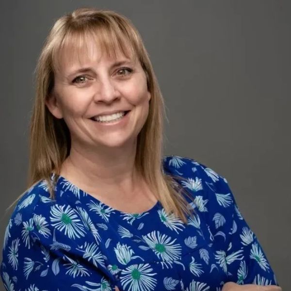 Smiling woman with blonde hair wearing a blue floral blouse.