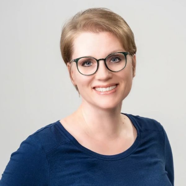 Smiling woman with glasses and short blonde hair in a navy blue top.