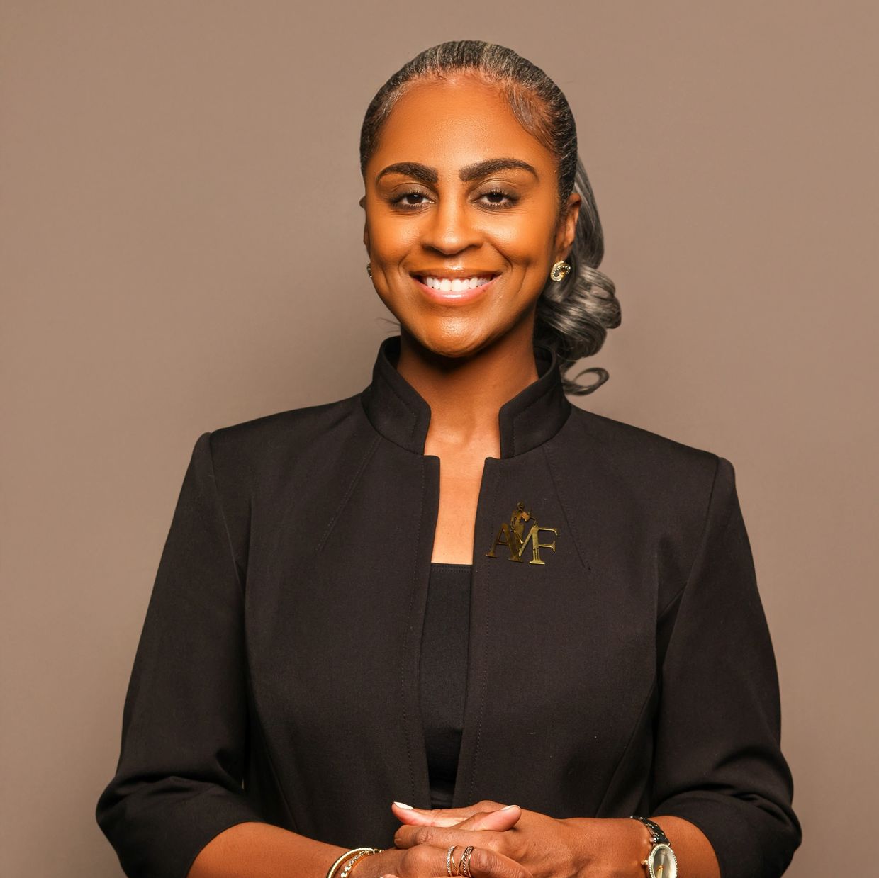 Confident woman in a black outfit smiling with hands clasped.