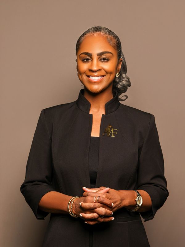 Confident woman in a black outfit smiling with hands clasped.