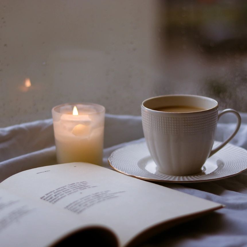 A cozy setup with a candle, coffee cup, and open book.