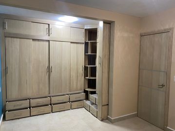 Modern wooden wardrobe with multiple drawers and corner shelves in a beige room.