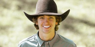 Young man smiling outdoors wearing a large black cowboy hat.