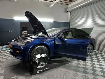 Blue Tesla Model 3 on ramp with Xpel wheel covers ready for PPF