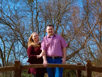 Couple posing on a wooden bridge in a park.