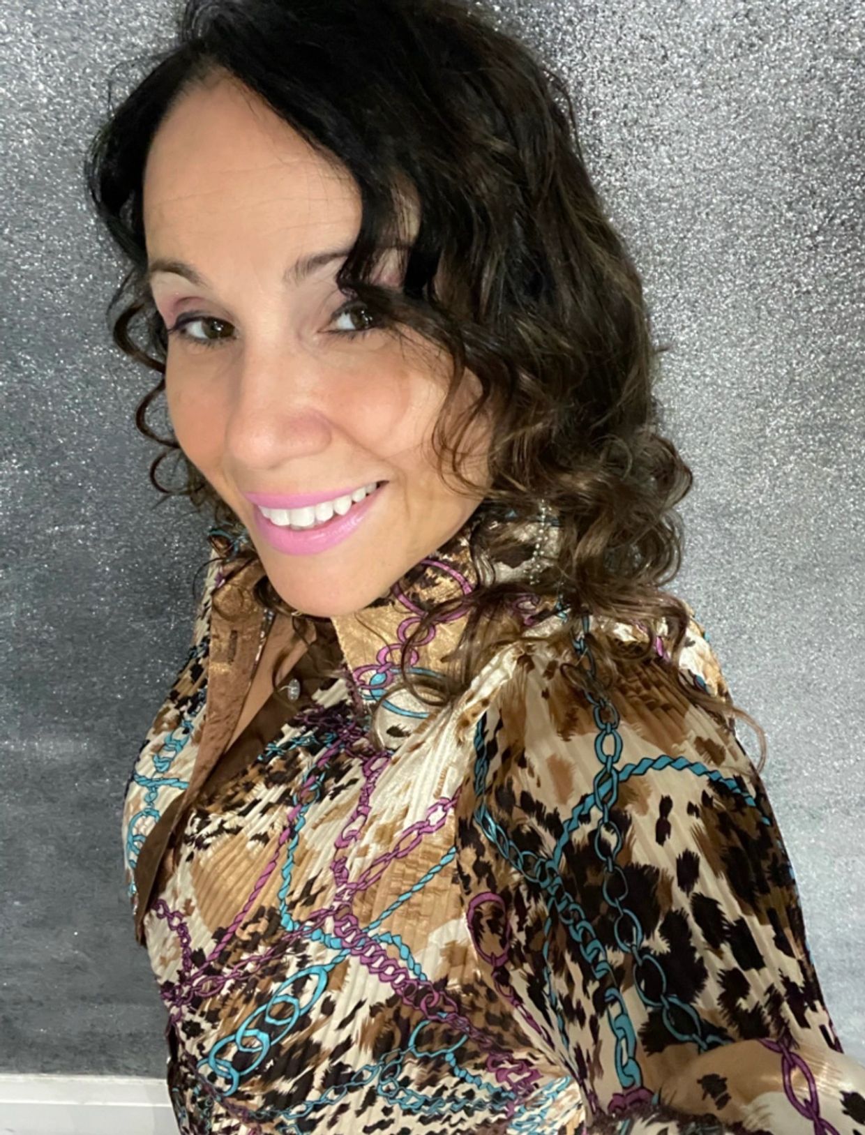 Smiling woman wearing a patterned blouse with curly hair.